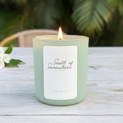 Green candle with a label on a wooden table with a blurred green foliage background